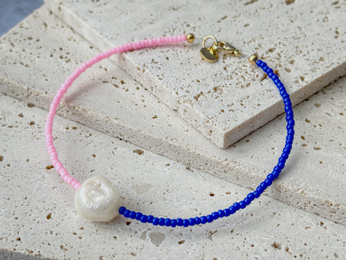 Handmade colorful beaded bracelet with pink and blue glass beads and a white freshwater pearl, displayed on a textured stone surface.